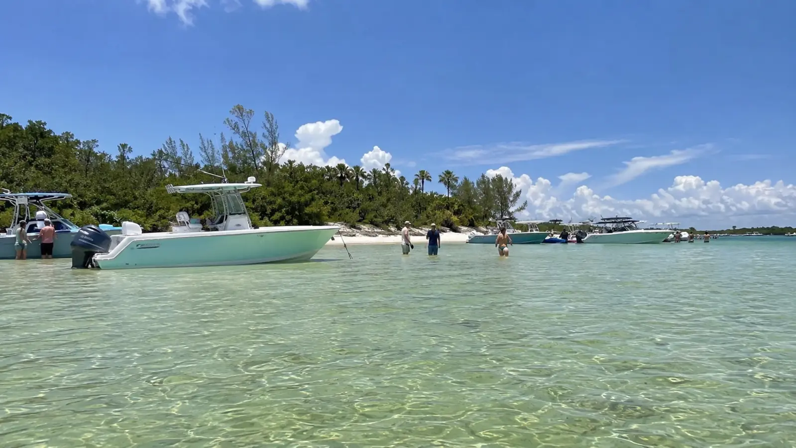 Boats anchored in shallow turquoise water near a sandy coastal shoreline